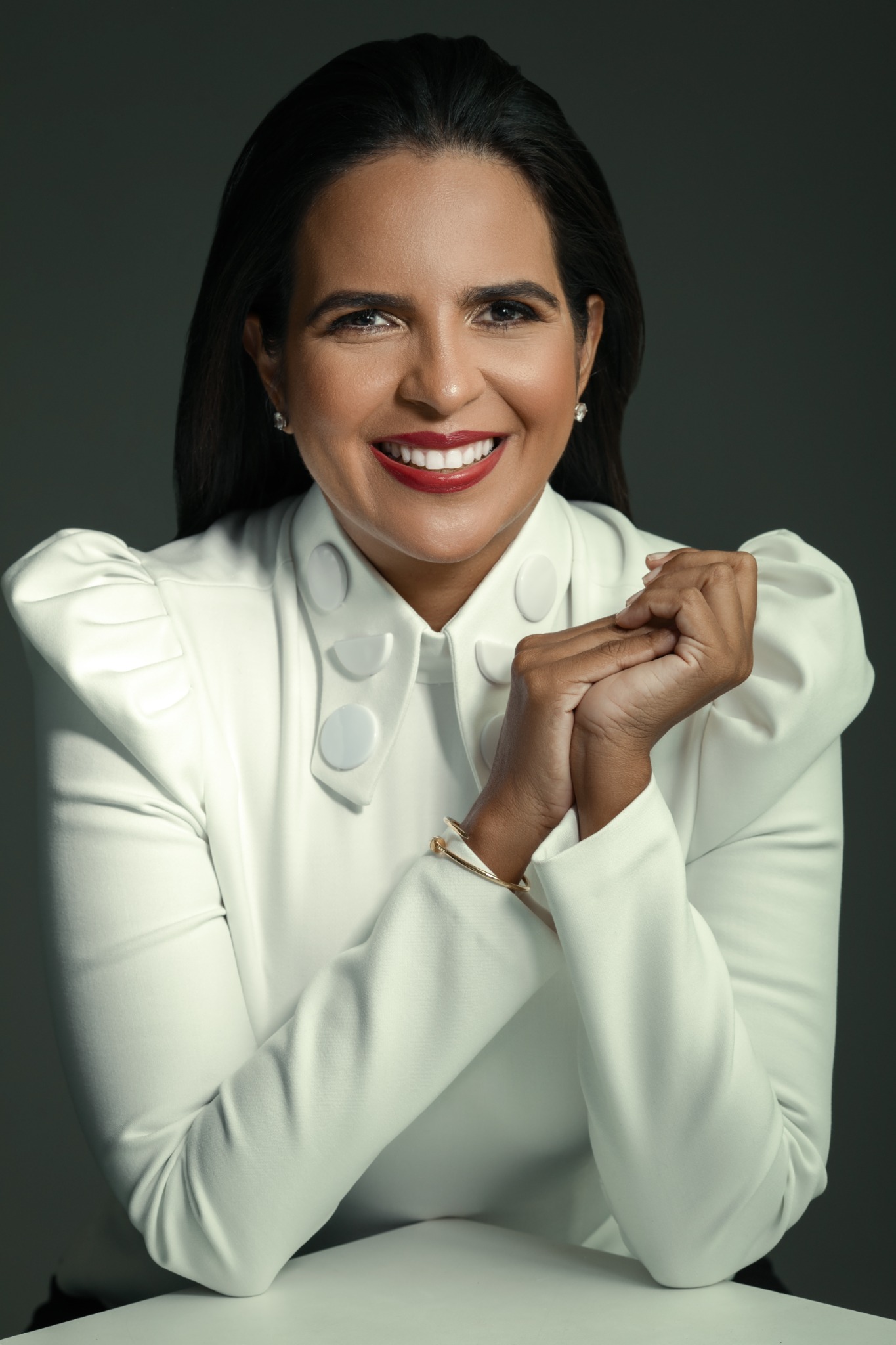 Janis Santaella sonriente con chaqueta blanca sobre fondo oscuro